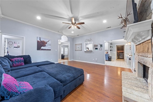 living room with ceiling fan, ornamental molding, a fireplace, and light hardwood / wood-style flooring