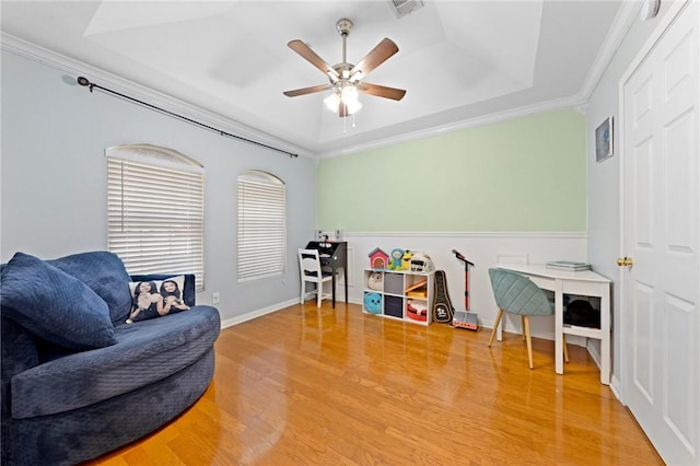 living area with a raised ceiling, ceiling fan, hardwood / wood-style floors, and ornamental molding