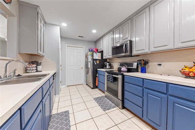 kitchen with appliances with stainless steel finishes, light tile patterned floors, blue cabinets, and sink