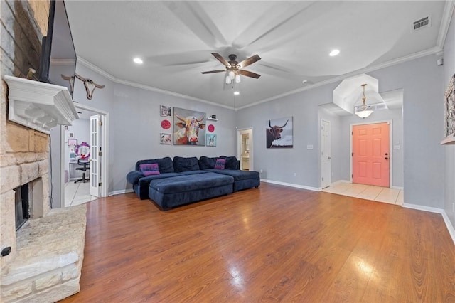 living room with ceiling fan, a stone fireplace, light wood-type flooring, and ornamental molding