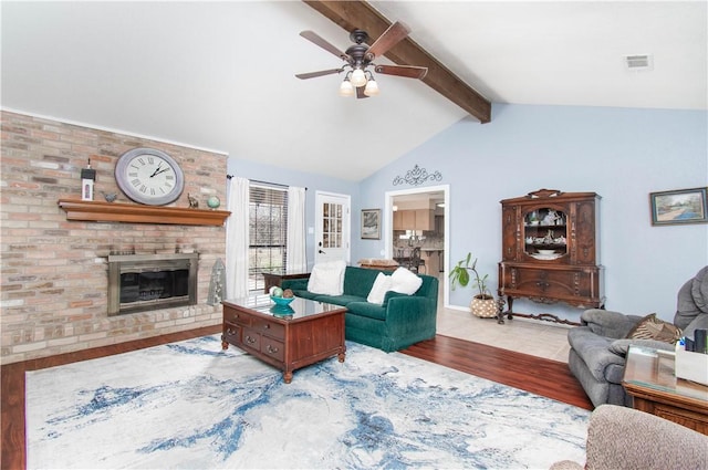 living area featuring vaulted ceiling with beams, visible vents, a ceiling fan, a brick fireplace, and wood finished floors