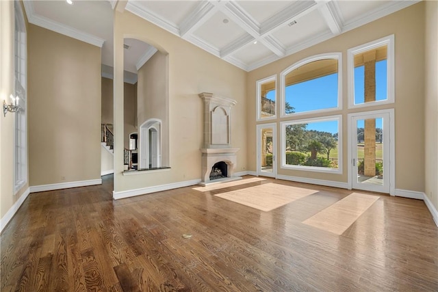 unfurnished living room with coffered ceiling, wood-type flooring, crown molding, a towering ceiling, and beamed ceiling