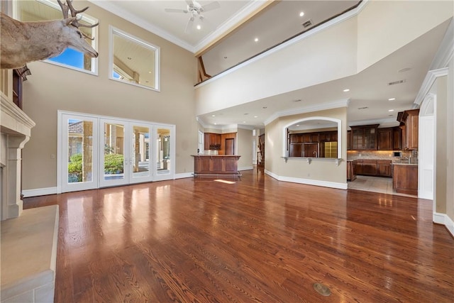 unfurnished living room featuring a healthy amount of sunlight, ceiling fan, crown molding, and a high ceiling