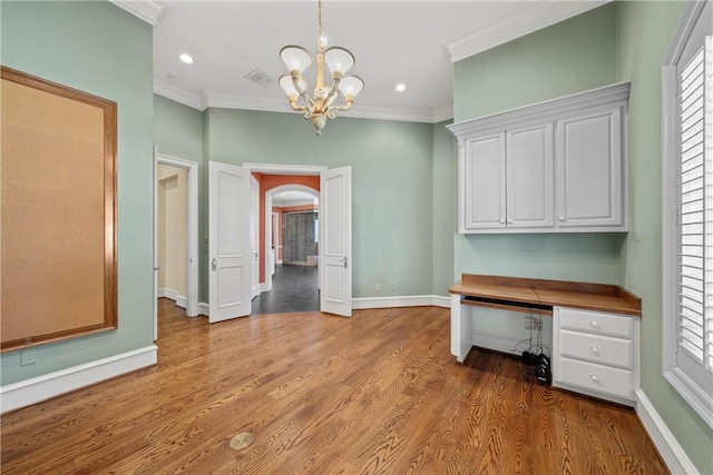 unfurnished office featuring ornamental molding, built in desk, light hardwood / wood-style floors, and a wealth of natural light