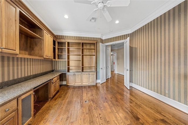 unfurnished office featuring built in desk, ceiling fan, dark hardwood / wood-style flooring, and crown molding