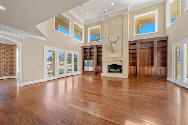 unfurnished living room with a fireplace, ceiling fan, ornamental molding, wood-type flooring, and a high ceiling