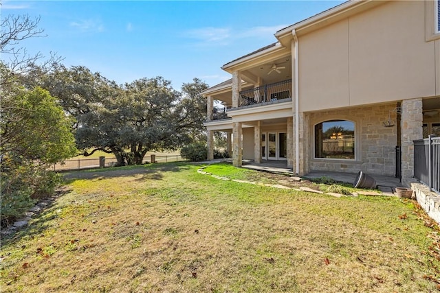 view of yard featuring a balcony, ceiling fan, and a patio