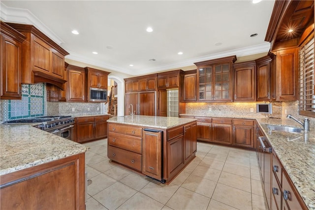 kitchen featuring sink, an island with sink, crown molding, and light stone countertops