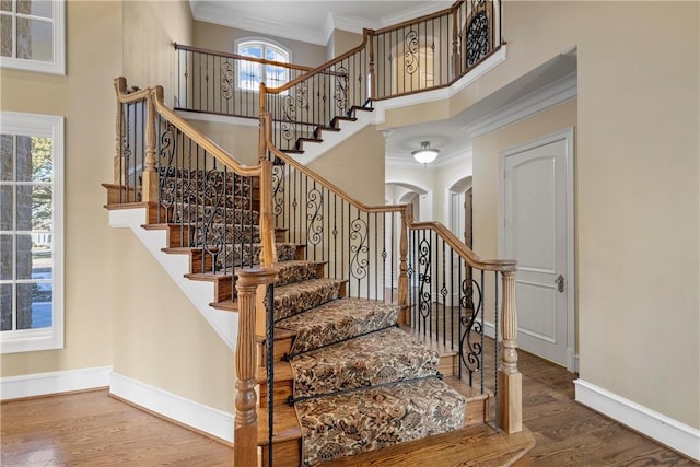 stairway with a high ceiling, ornamental molding, and hardwood / wood-style floors