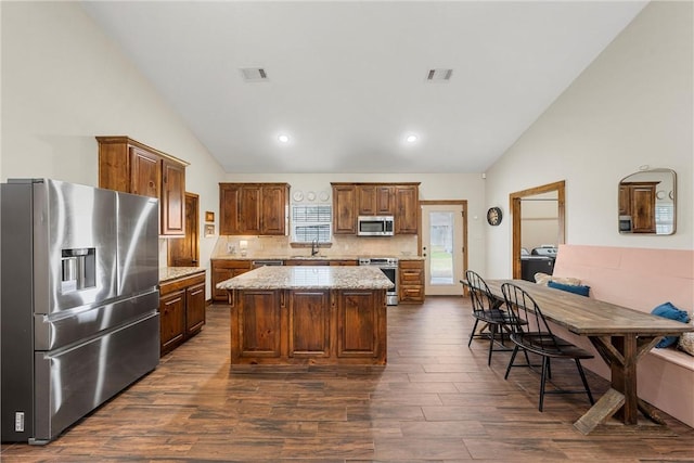 kitchen with a center island, light stone counters, decorative backsplash, stainless steel appliances, and dark wood-style flooring