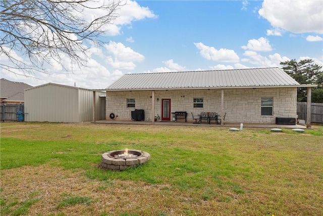 back of property featuring a lawn, metal roof, a fire pit, and fence