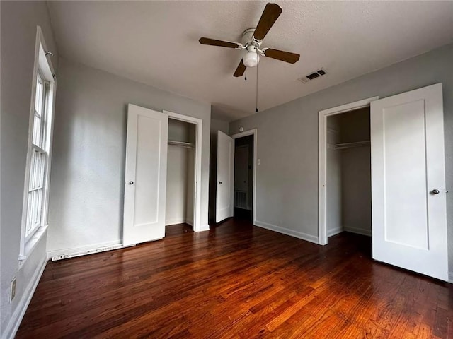 unfurnished bedroom with dark hardwood / wood-style flooring, two closets, and ceiling fan