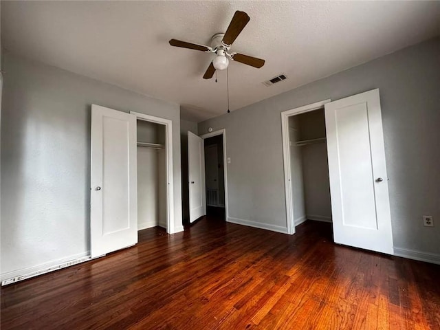 unfurnished bedroom featuring dark hardwood / wood-style flooring, two closets, and ceiling fan