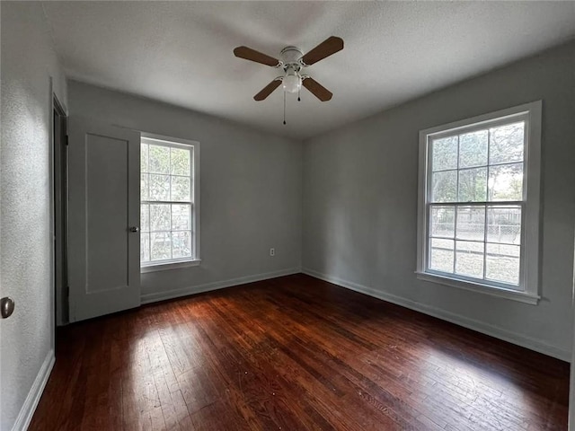 empty room featuring ceiling fan, dark wood-type flooring, and a wealth of natural light