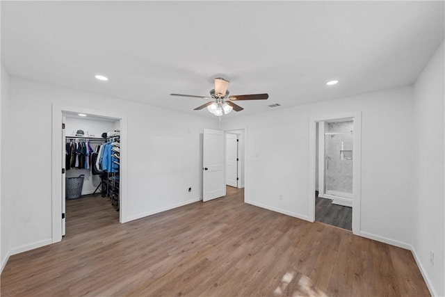 unfurnished bedroom featuring connected bathroom, ceiling fan, wood-type flooring, a walk in closet, and a closet