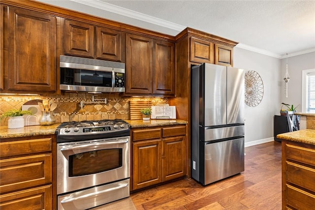 kitchen featuring crown molding, decorative backsplash, light stone countertops, light hardwood / wood-style floors, and stainless steel appliances