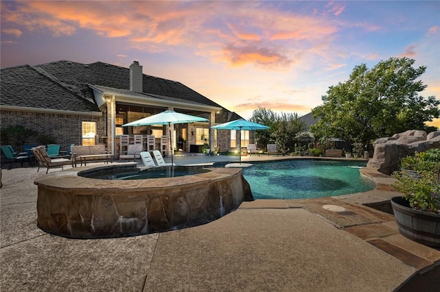 pool at dusk with an in ground hot tub, pool water feature, a patio, and an outdoor hangout area