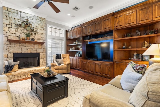 living room featuring light hardwood / wood-style floors, a stone fireplace, ceiling fan, and crown molding