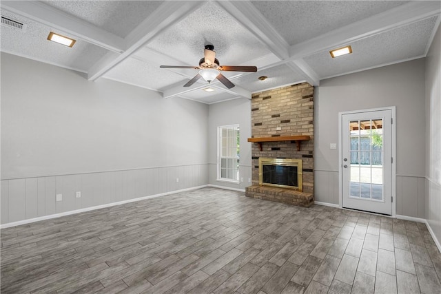 unfurnished living room featuring a brick fireplace, wainscoting, a textured ceiling, and beamed ceiling