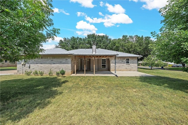 rear view of house featuring metal roof, a patio, brick siding, a lawn, and a chimney