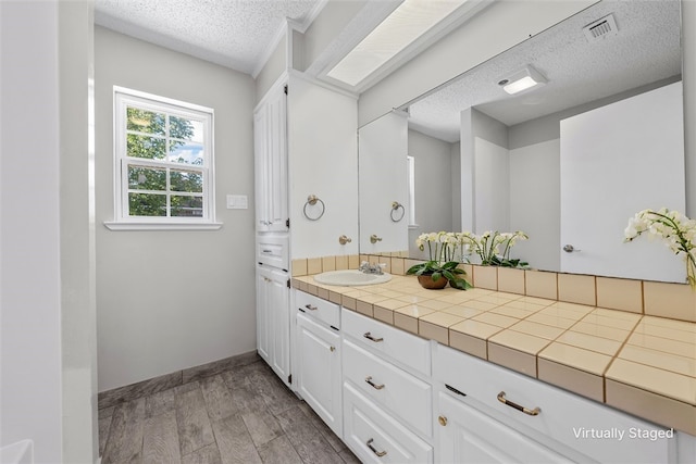 bathroom featuring a textured ceiling, wood finished floors, vanity, visible vents, and baseboards