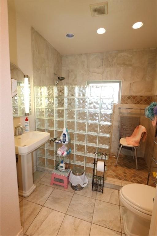 bathroom featuring tile patterned flooring, toilet, a tile shower, and tile walls