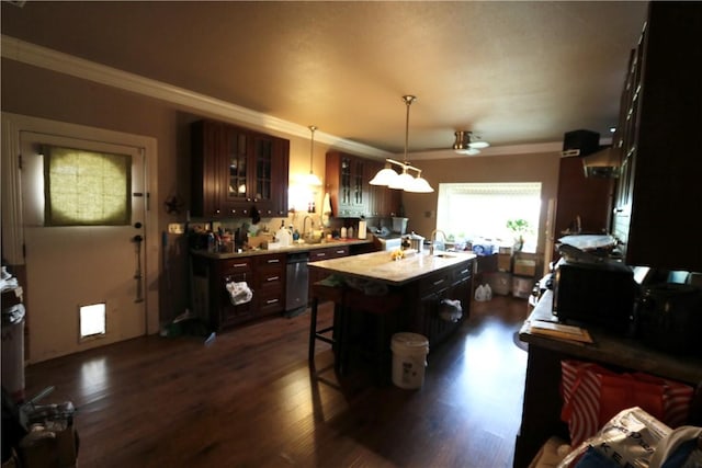 kitchen featuring dark wood-type flooring, crown molding, an island with sink, decorative light fixtures, and a kitchen bar