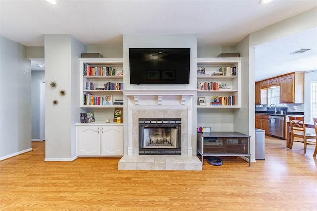 living room with visible vents, baseboards, light wood-style flooring, and a tiled fireplace