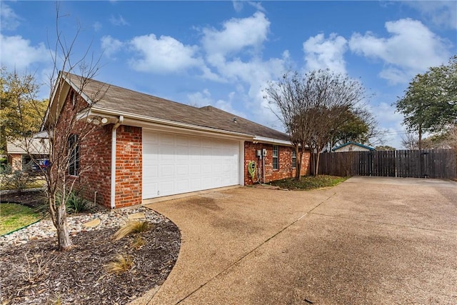 view of side of property featuring brick siding, driveway, an attached garage, and fence