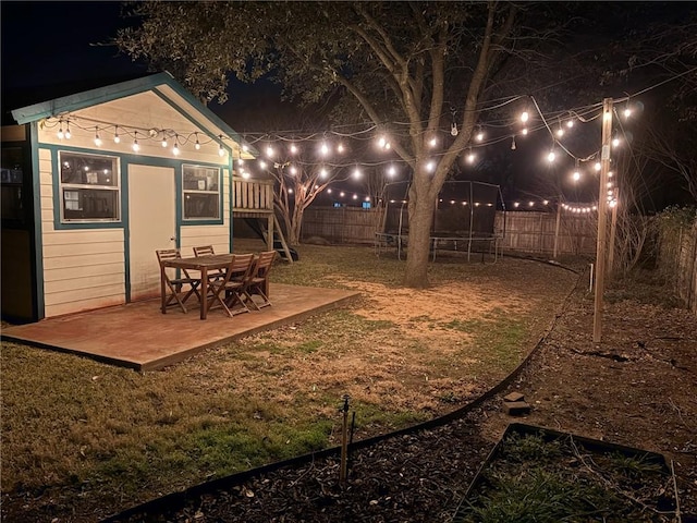 yard at night featuring a patio area, a trampoline, a fenced backyard, and an outdoor structure