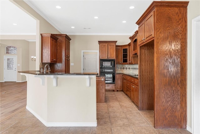 kitchen featuring black appliances, dark stone countertops, light tile patterned floors, a kitchen bar, and kitchen peninsula