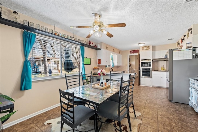 dining space with ceiling fan, dark tile patterned floors, and a textured ceiling