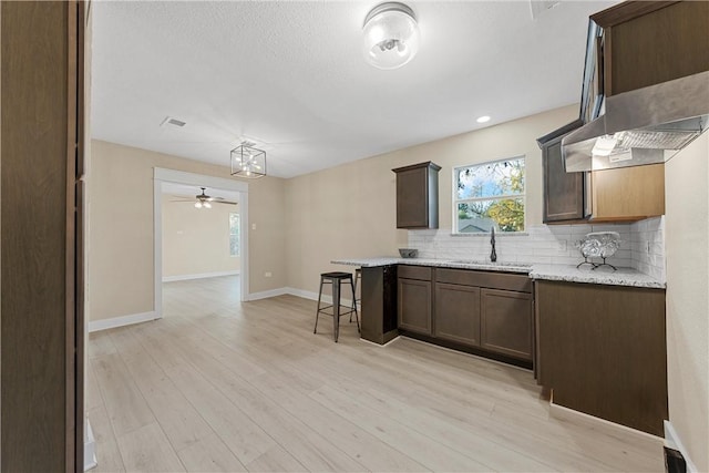 kitchen featuring light wood-type flooring, light stone counters, a breakfast bar area, and sink