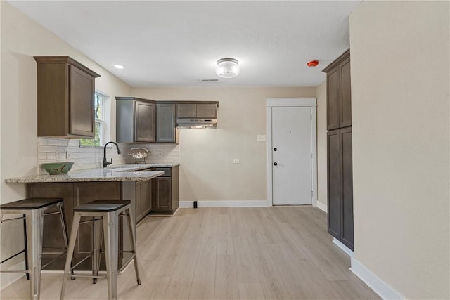 kitchen with light stone countertops, sink, tasteful backsplash, a breakfast bar area, and light wood-type flooring