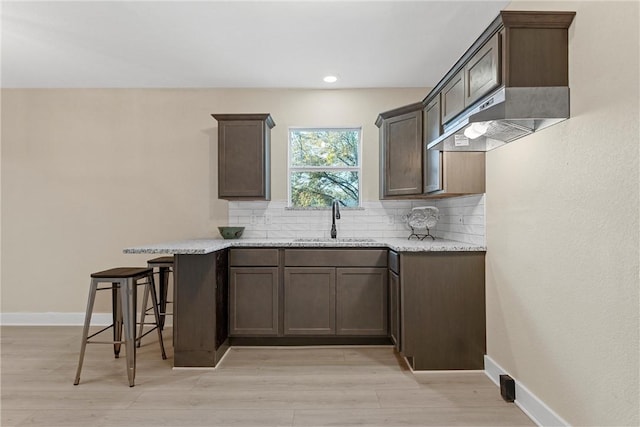 kitchen featuring a breakfast bar, sink, light wood-type flooring, tasteful backsplash, and light stone counters