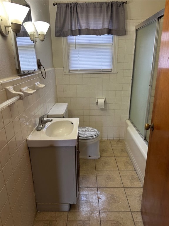 bathroom featuring vanity, tile walls, toilet, and bath / shower combo with glass door