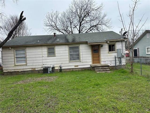 back of house featuring a yard, central AC unit, a shingled roof, and fence