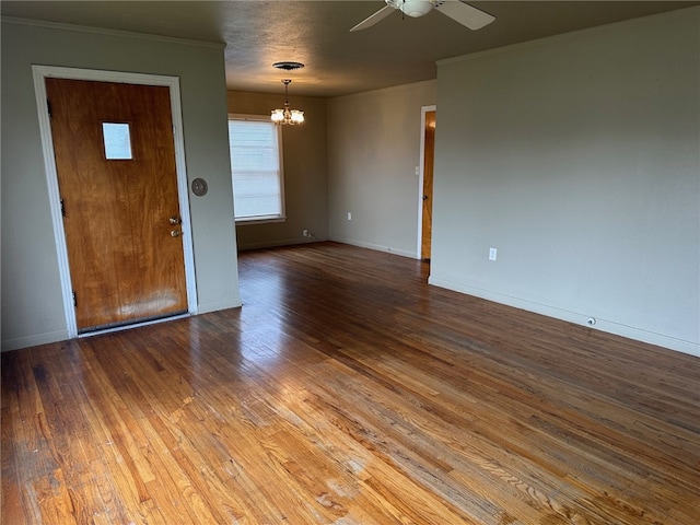 empty room with ceiling fan with notable chandelier, crown molding, baseboards, and wood-type flooring