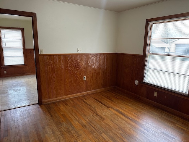 empty room with wood finished floors, a wainscoted wall, and wood walls