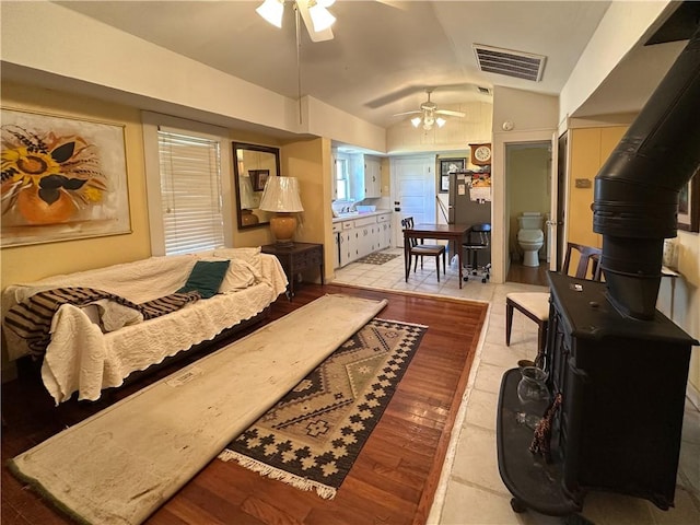 living area featuring a wood stove, ceiling fan, visible vents, and vaulted ceiling