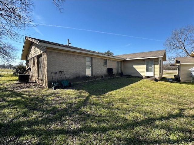 back of house with entry steps, a yard, central air condition unit, and brick siding