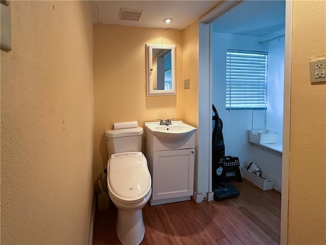 half bathroom featuring visible vents, vanity, toilet, and wood finished floors