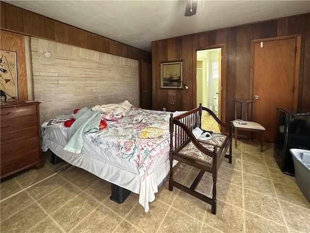 bedroom featuring wood walls, ensuite bath, brick wall, and ceiling fan