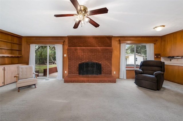 carpeted living room with a brick fireplace, ceiling fan, a healthy amount of sunlight, and wood walls