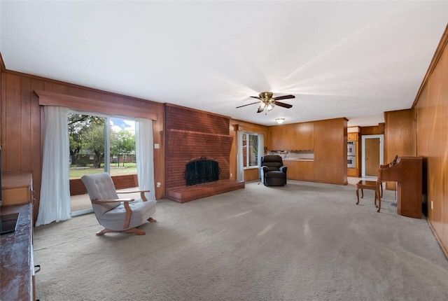 carpeted living room with wooden walls, ceiling fan, ornamental molding, and a brick fireplace