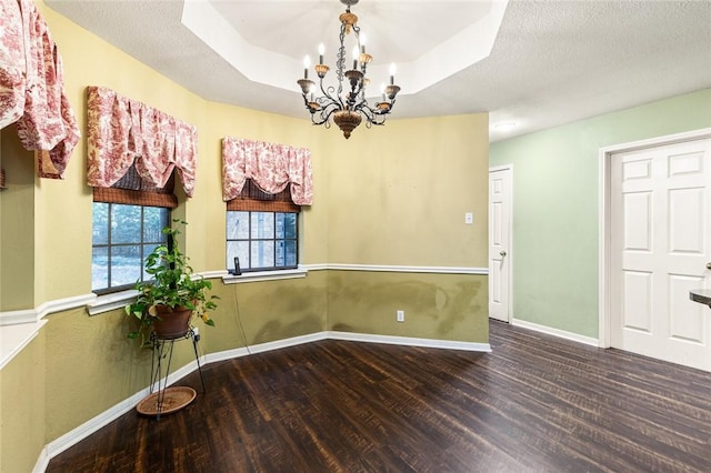 unfurnished dining area featuring a raised ceiling, dark hardwood / wood-style flooring, a textured ceiling, and an inviting chandelier