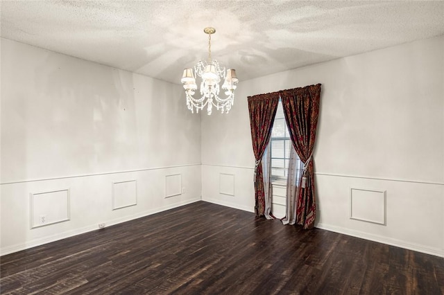 spare room with a textured ceiling, a chandelier, and dark hardwood / wood-style floors