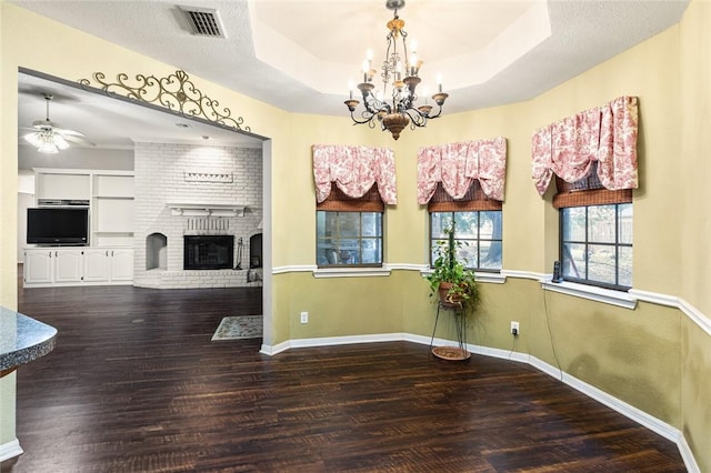 dining area featuring ceiling fan with notable chandelier, a raised ceiling, a brick fireplace, dark hardwood / wood-style floors, and built in features