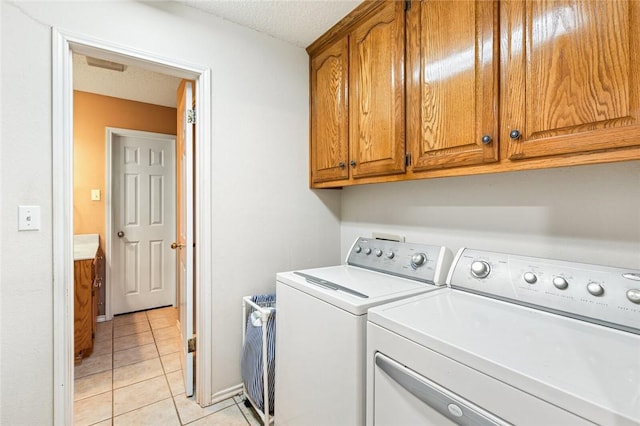 clothes washing area featuring washing machine and dryer, light tile patterned floors, cabinets, and a textured ceiling