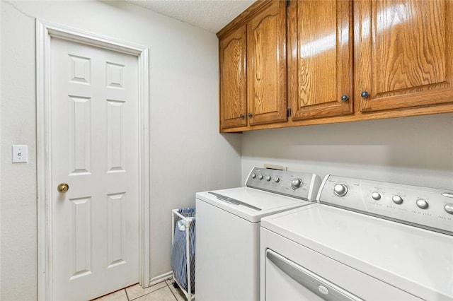 clothes washing area with washer and dryer, light tile patterned flooring, cabinets, and a textured ceiling